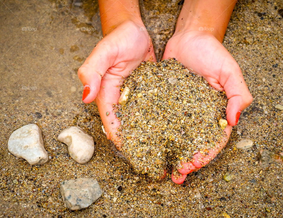 Hands of a woman resting on the sea beach and playing with sand and stones