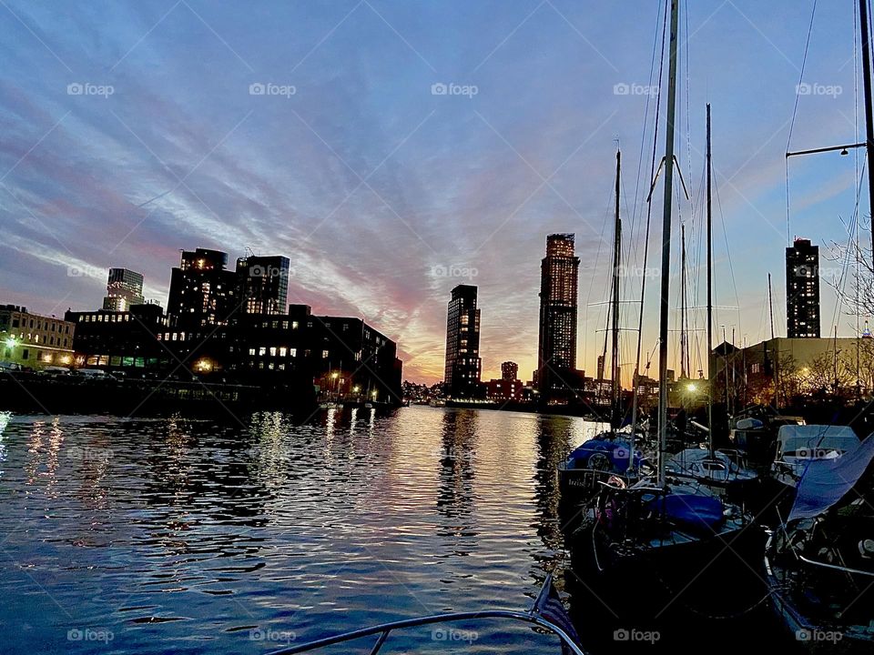Newtown Creek in the twilight hours with the setting sun at the horizon and the silhouettes of high rise city buildings. The sailboats with their tall masts in the foreground add nicely to the composition. 2021. Hypnotic Productions