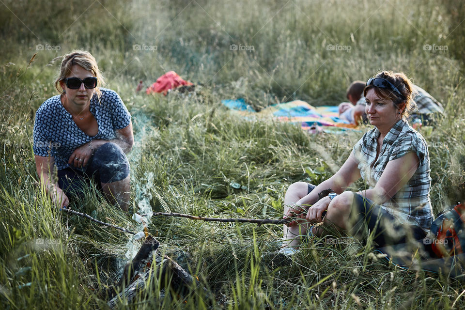 Women roasting a marshmallows over a campfire on meadow. Vacations close to nature. Candid people, real moments, authentic situations