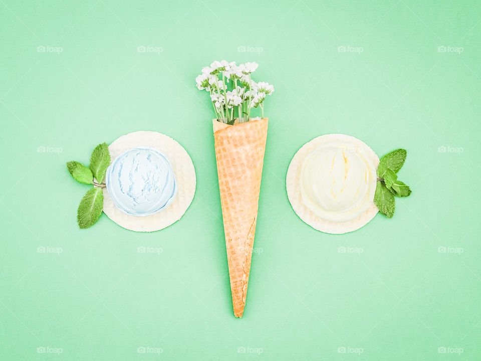 Two balls of berry ice cream on round wafers and one wafer cone with flowers lie in the center on a green background, flatley close-ups. Concept summer treat, summer food, natural ice cream.