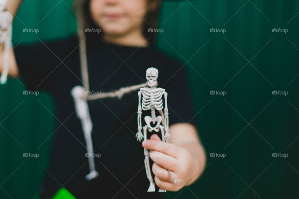 A girl in a witch costume on a green background holds a skeleton in her hands. Halloween concept