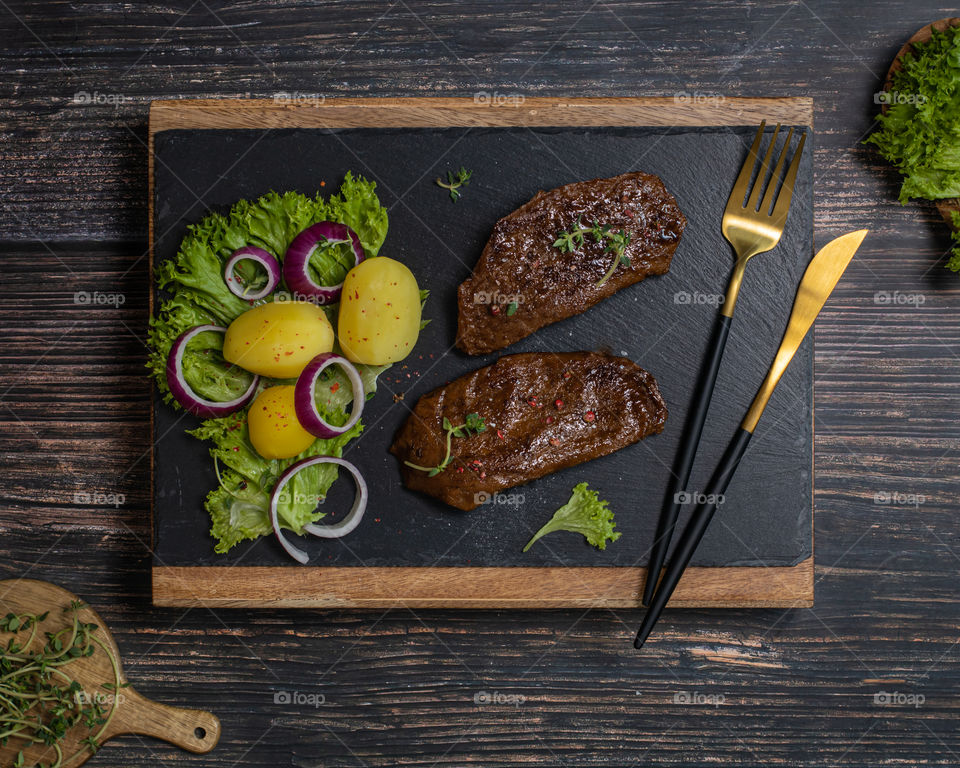 Vegan steak kn a black plate served with potatoes and fresh salad 