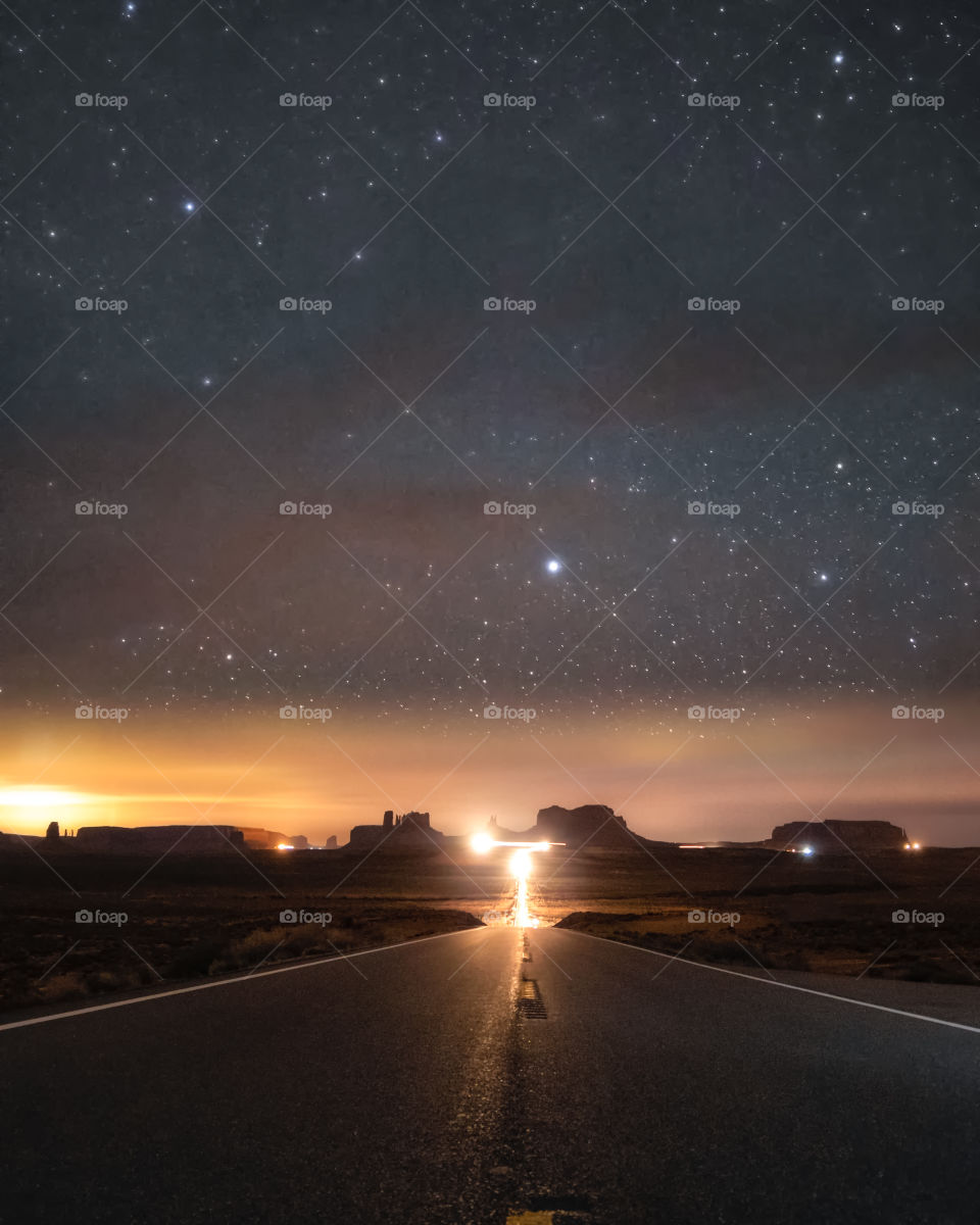 Stars poking through as clouds streak across the night sky above the road leading to monument valley, seen from forest Gump point.