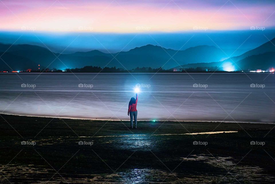 woman lighting with her flashlight at the shore of a lake