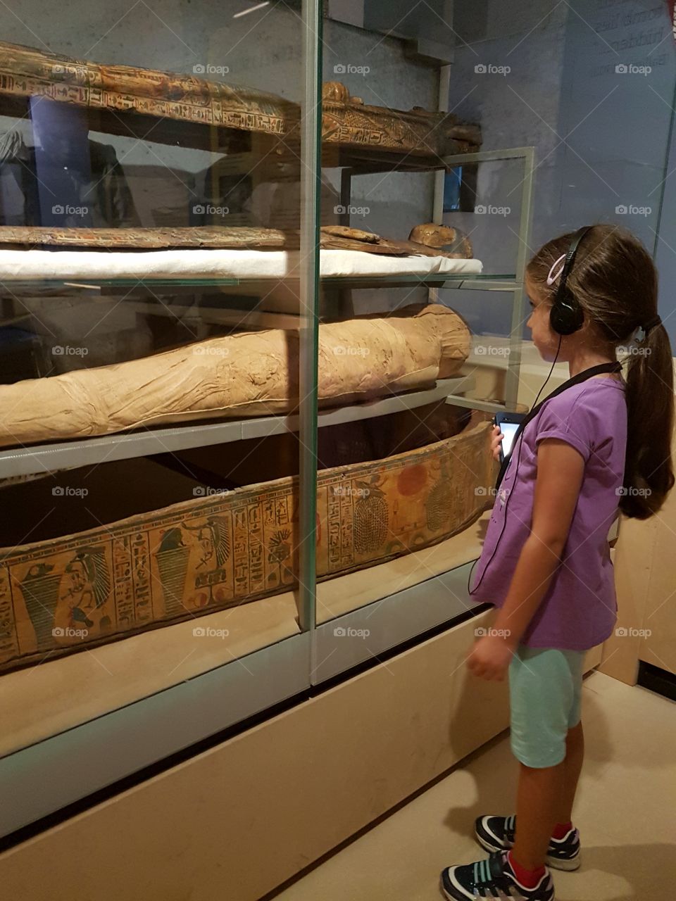 Little girl listening to the audioguide in front of the mummies of the Egyptian museum in