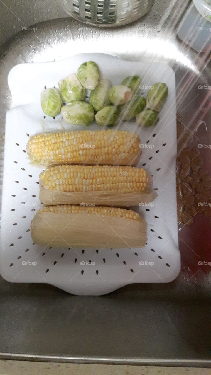 Brussel sprouts and peaches and cream corn on the cob under running water