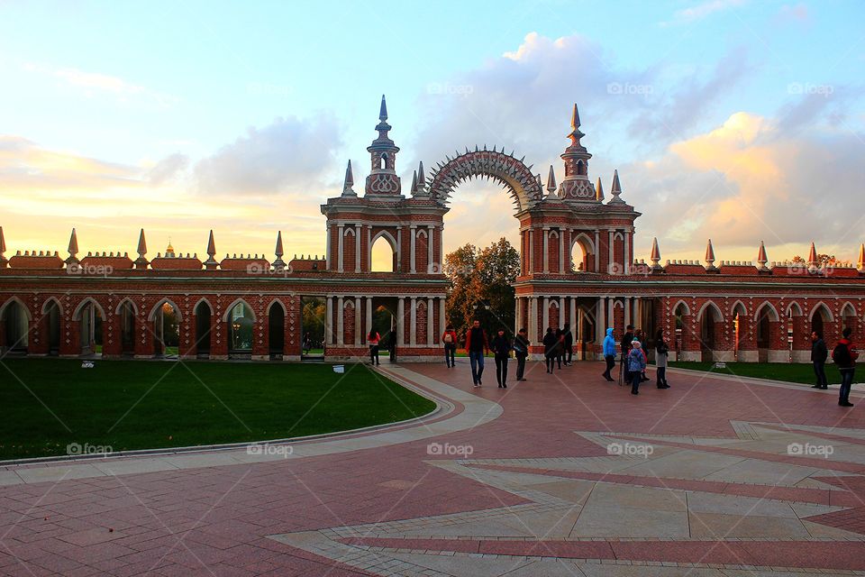 Wonderful sunset over Tsaritsyno park gate's entry, red brick arch, people walking