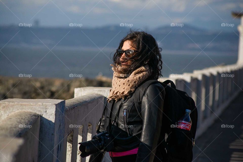 young curly woman with her camera around her neck watching the sea