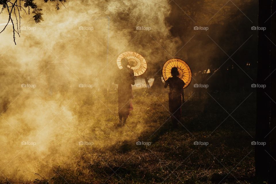silhouette of two monks running through smoke with orange decorated umbrellas in Myanmar 