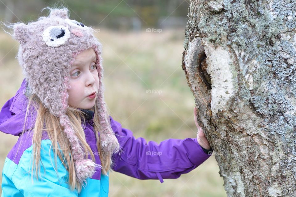 Little girls enjoying outdoors . Little girl with hat on looking at a tree 