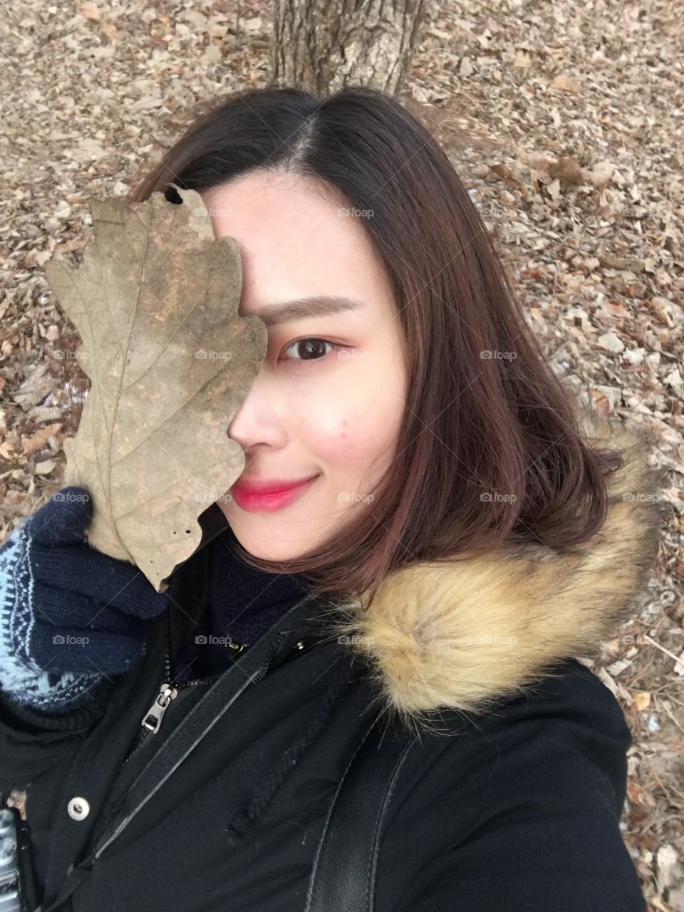 Young girl covered her face with dry autumn leaf