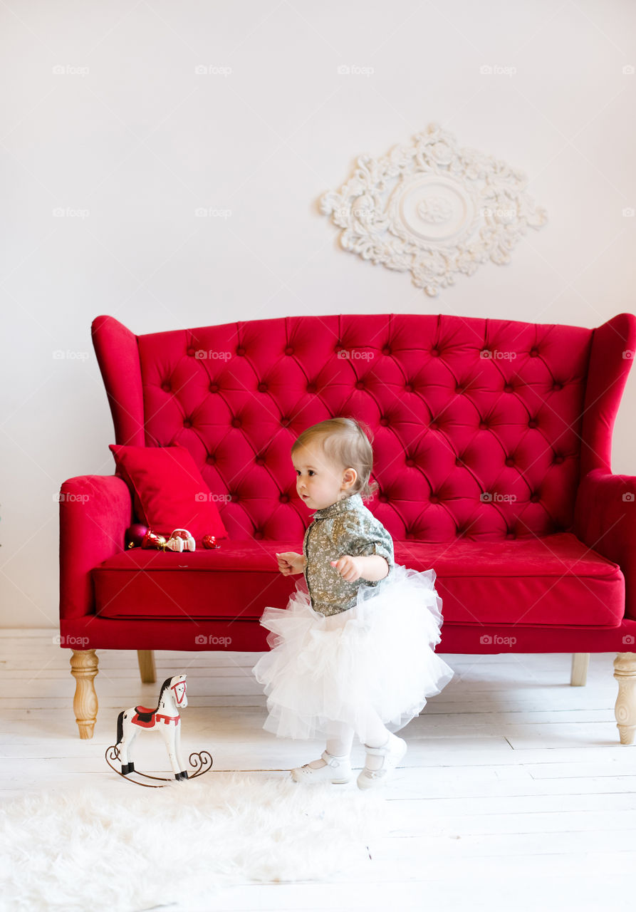 Cute toddler walking near red sofa in house