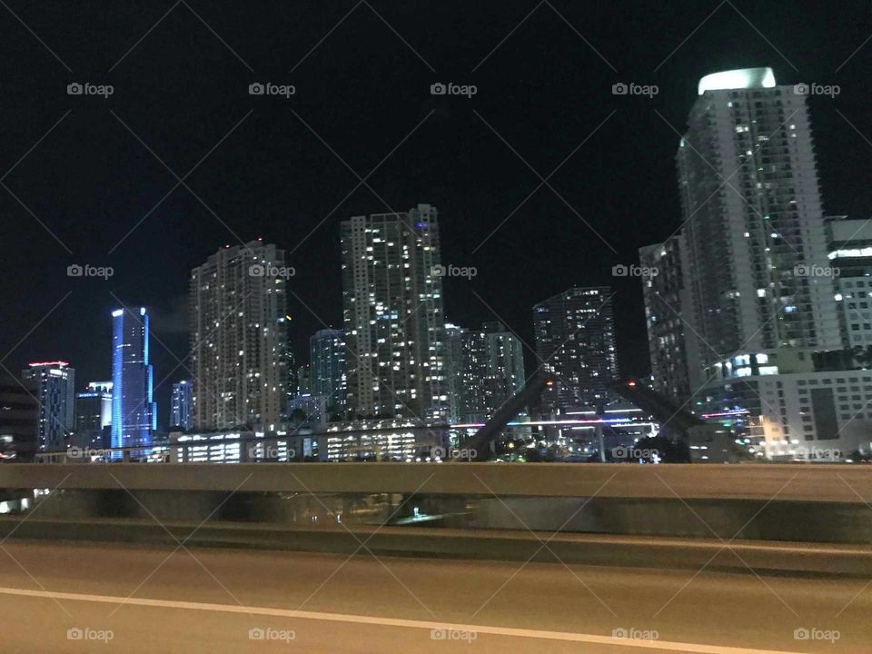 Downtown Miami and transit rail at
 night. Miami skyline in the nighttime lit up on a clear summer night in 2017. Neon lights and skyscraper lights. Great view of the city of Miami from a bridge while moving in car.