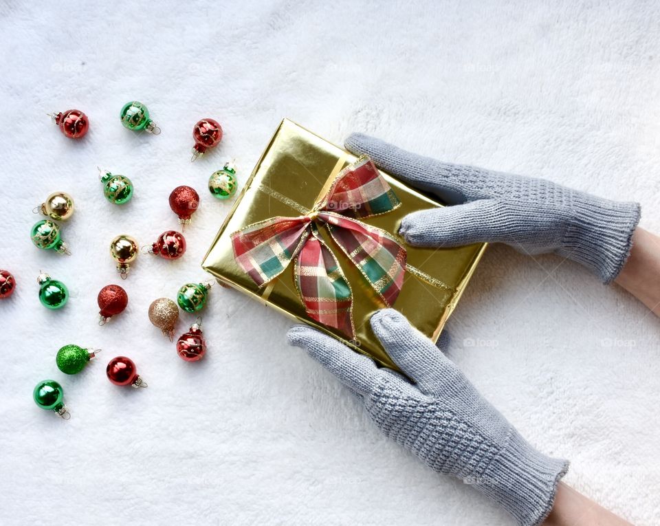 Flat lay still life with a Christmas theme, hands with gloves on holding a package and colorful ornaments 