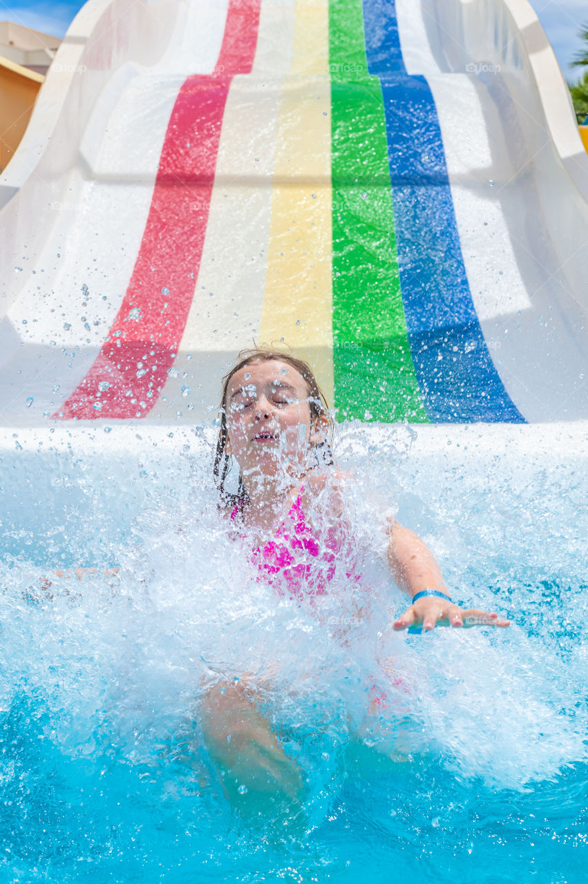 Little girl on rainbow coloured water slide.