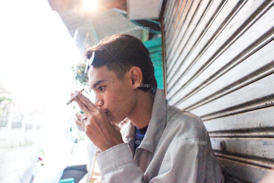 Young man smoking cigarette while sitting on window sill