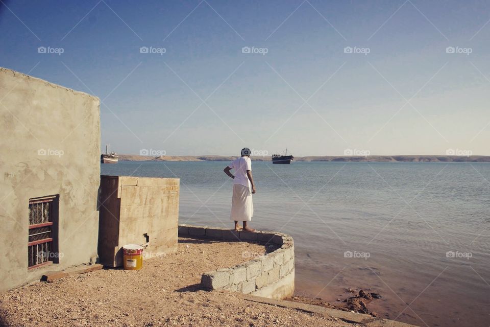 Omani fisherman looks out onto the water after sunrise
