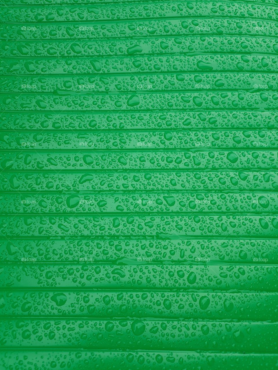 Close up of water droplets on a wet shiny plastic surface green with horizontale lines parallele