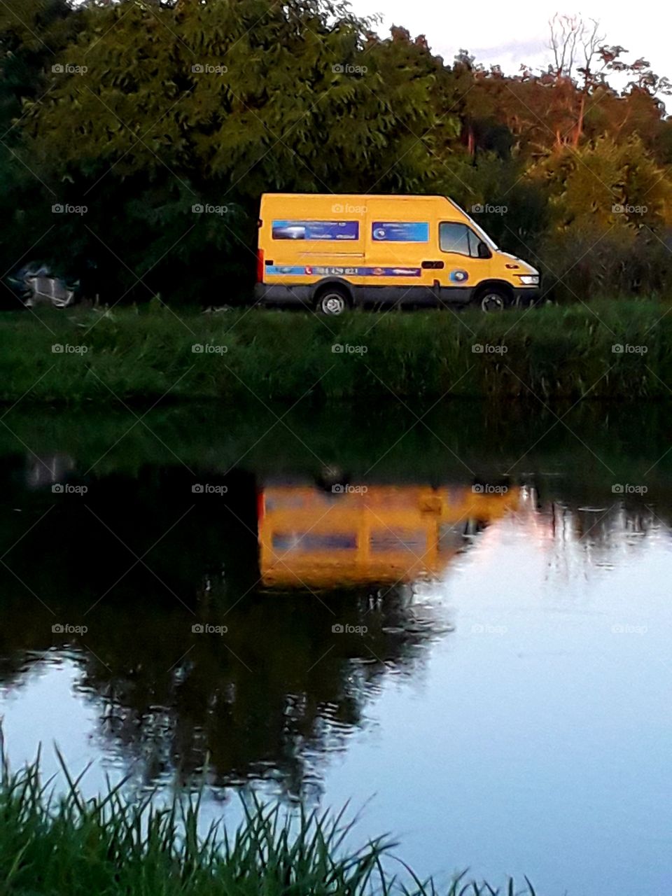 this is your road trip - yellow van parking by the pond reflected in water at golden hour