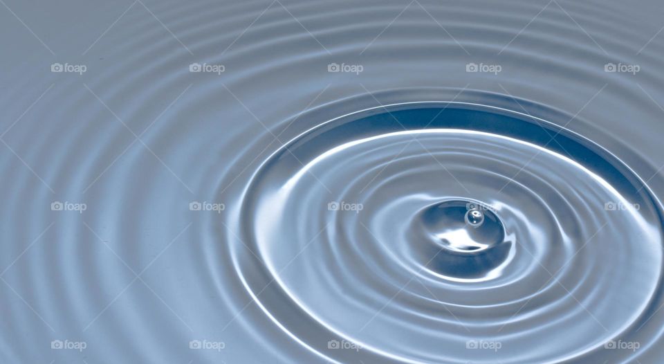 Falling water droplet creating round splash with ripples.