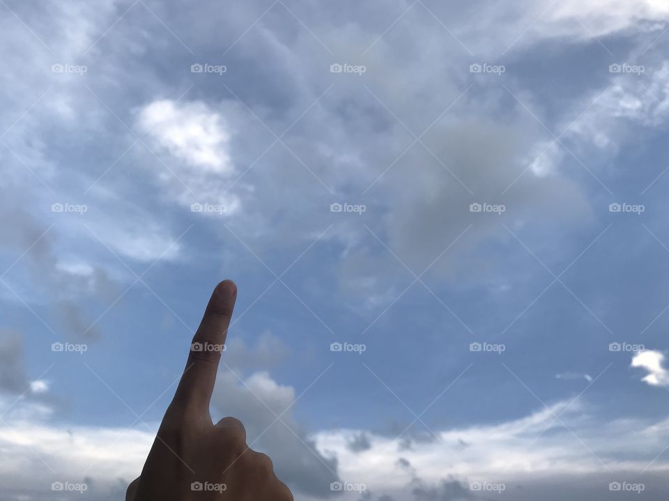 woman uses her right forefinger pointing up in the bright blue sky with white cloud in daylight with copy space on the top of frame