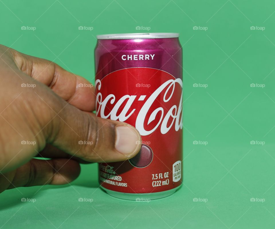 hand grabbing a can of cherry Coca-Cola with a green background
