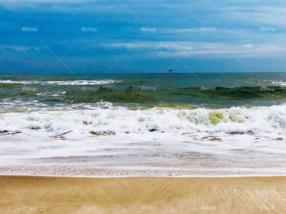 Blue sky with water rolling on the warm sand