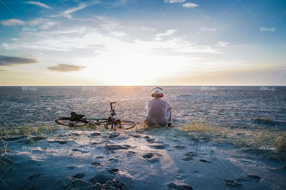 Man sitting next to his bike, om the beach, looking at  sunset