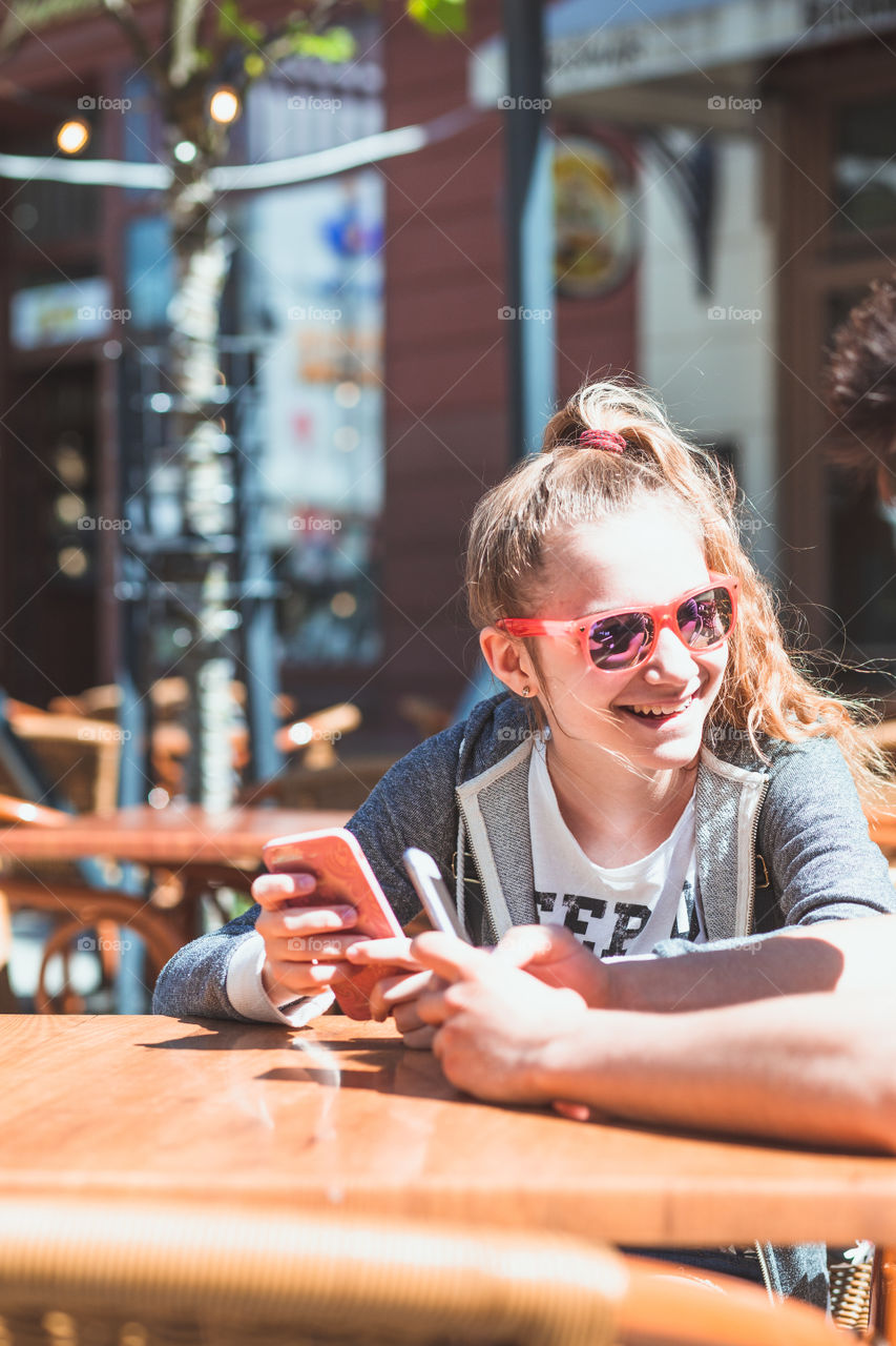 Young woman and man sitting in pavement cafe a the table talking and using mobile phones