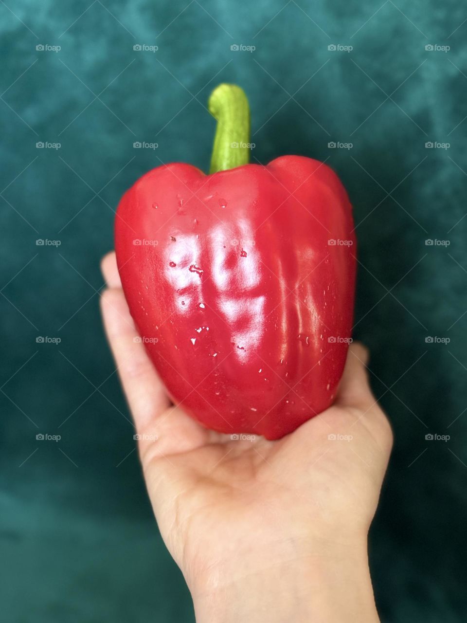 close up of juicy red paprika in hand on green velvet background