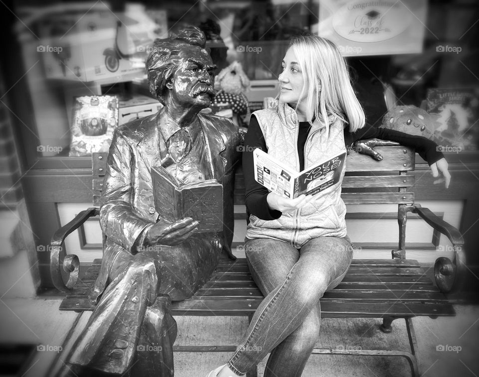 A casually dressed woman sits and poses with a statue of Mark Twain on a bench in Bellingham, Washington 