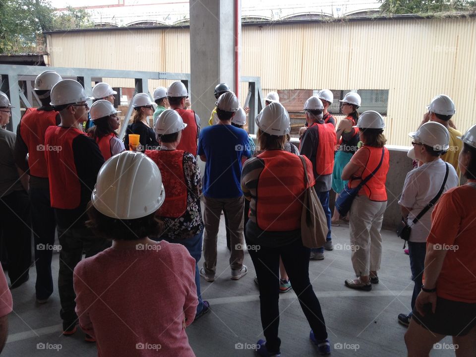 Crowd of people construction hard hats and vests listening to a construction site guide.