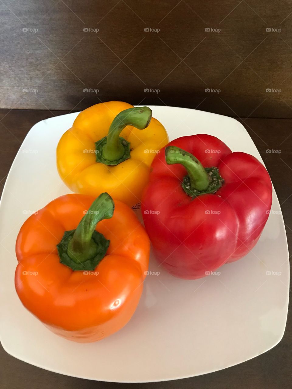 Peppers on a white plate - Image if three peppers - yellow, orange and red peppers 