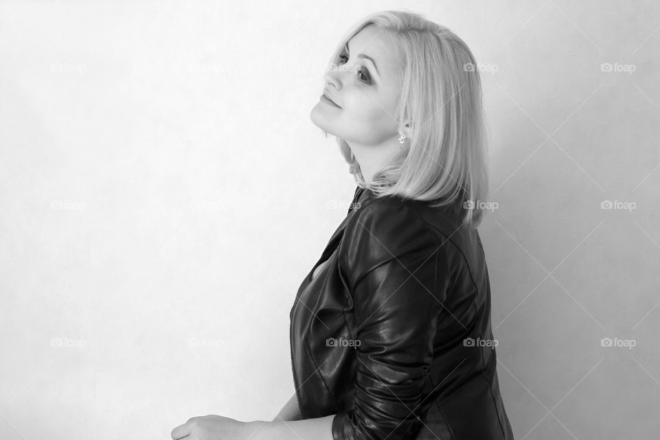 A blonde girl on a white background in a black leather jacket expresses her emotions and feelings (joy, sadness, amorousness, femininity, sensuality, tenderness)