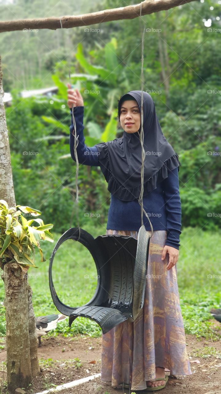 An Indonesian Muslim woman poses with a swing made from waste car tires