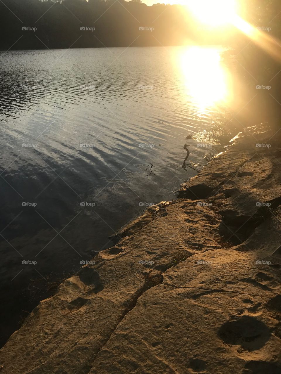 Sunset reflecting on lake surface with smooth stone shoreline