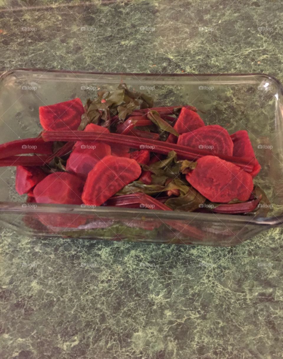 Display of reddish maroon beets with beautiful  beet greens in a glass dish on the countertop.