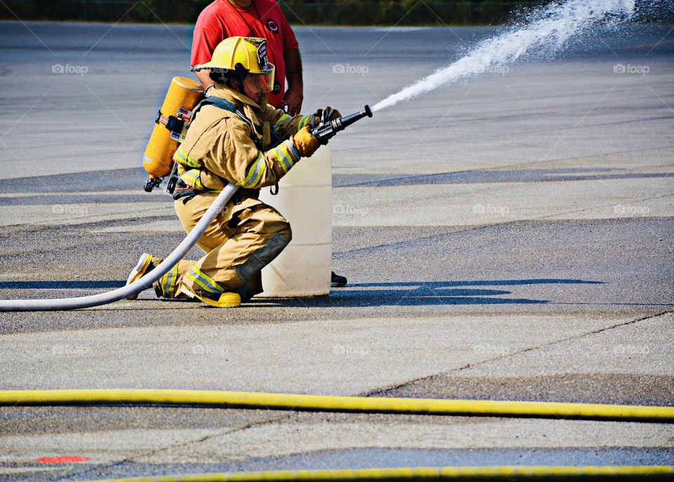 Liquids - A fire fighter in training practices using the water hose, directing water to the fire. 