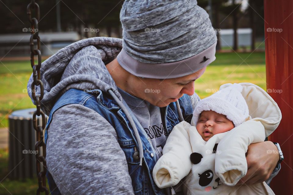 Mother holds daughter on her first park visit, mother holds newborn daughter, mother and daughter on swing, tender moments with newborn daughter 