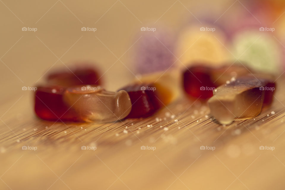 A macro portrait of some cola bottle shaped candy on a wooden table. It is sweet and delicious but unhealthy.