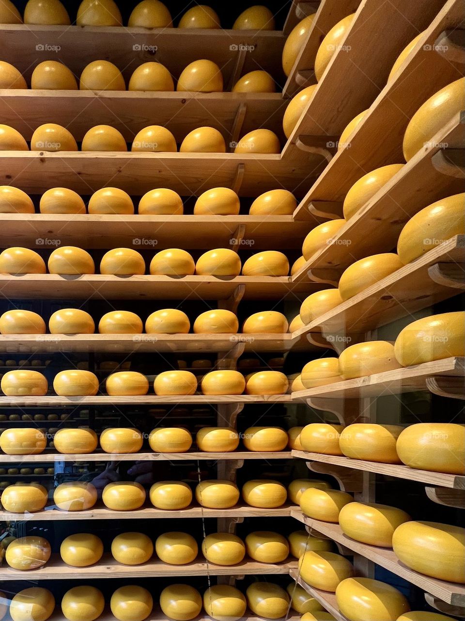 Yellow cheese heads neatly stacked on top of each other in a display case. The smooth texture and rich color make the composition attractive.
