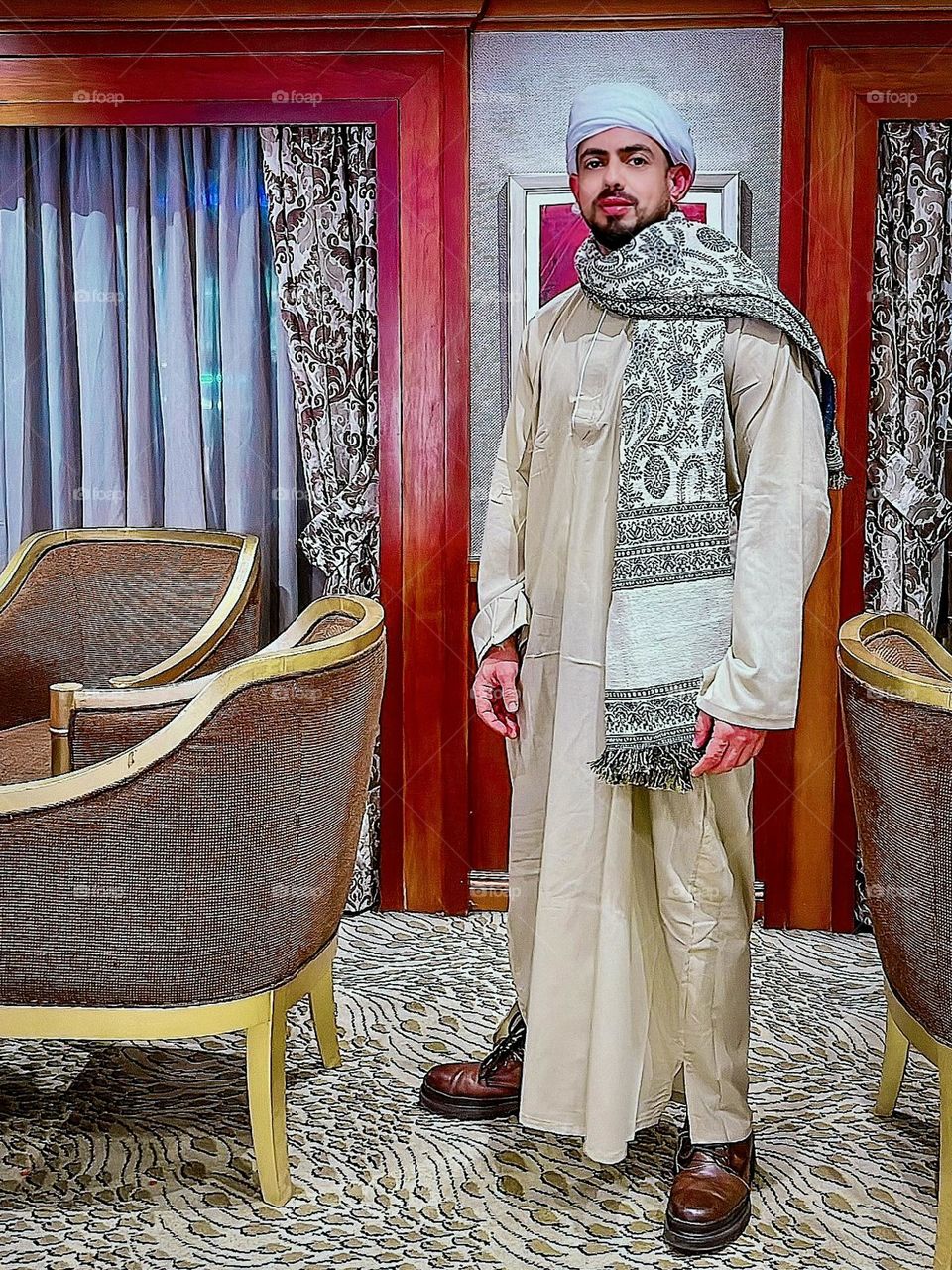 A man in traditional Upper Egyptian Sa'idi attire standing in an ornate room.