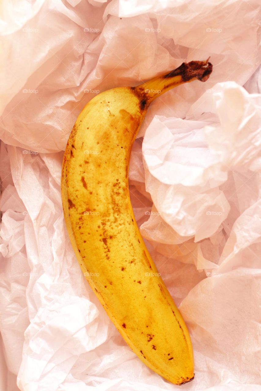 A banana with brown spots lies in peach-colored crumpled paper