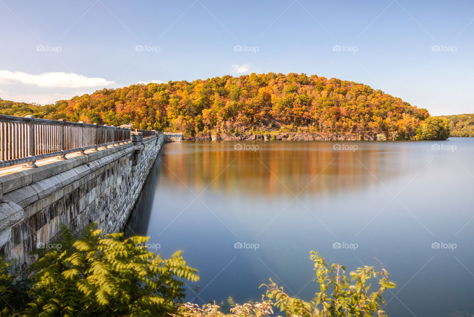 Beautiful fall foliage colors reflecting in a crystal clear still lake. Bridge walkway leading to the colorful wooded area. 