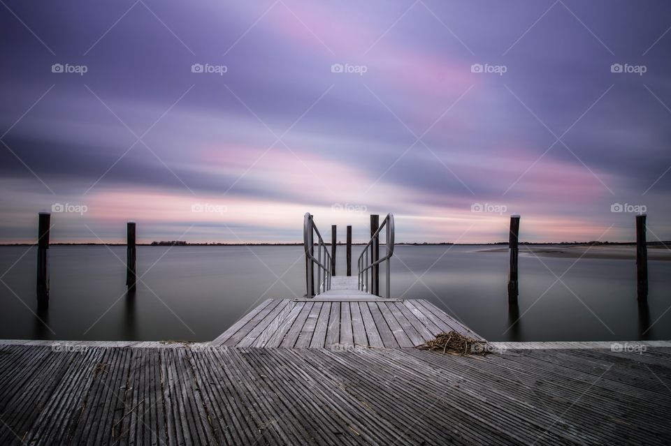 Pastel colors clouds sweep across the sky over an isolated pier. 