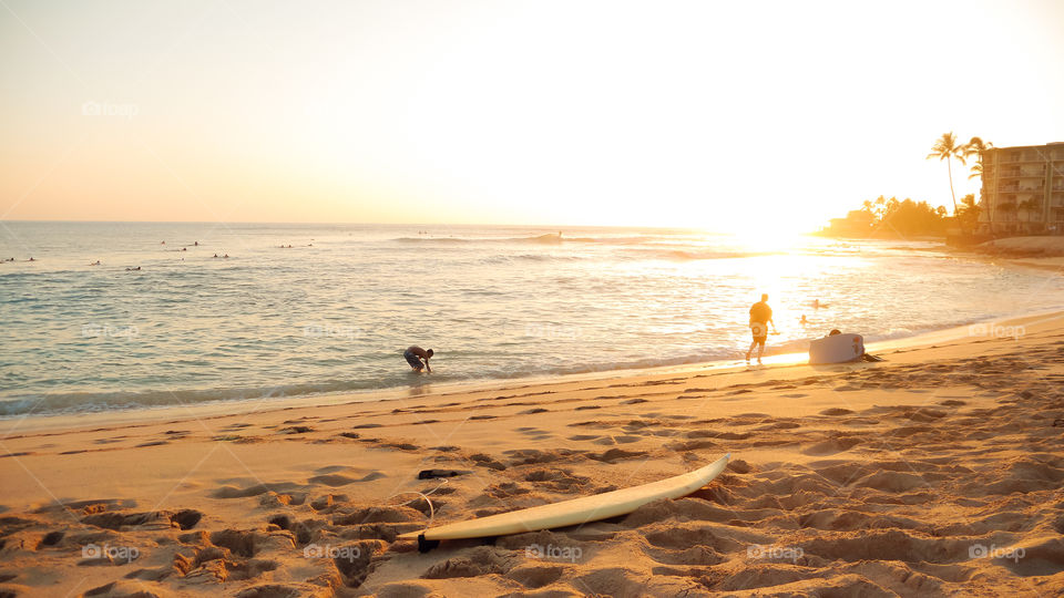 Tropical surf beach.  Surf board on the sand people on the background with the ocean during the magic hour. 
Makaha beach Hawaii Oahu 