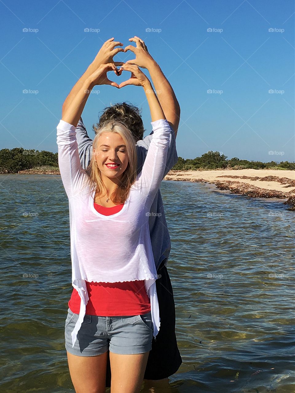 Young couple in water at beach making heart sign with hands 