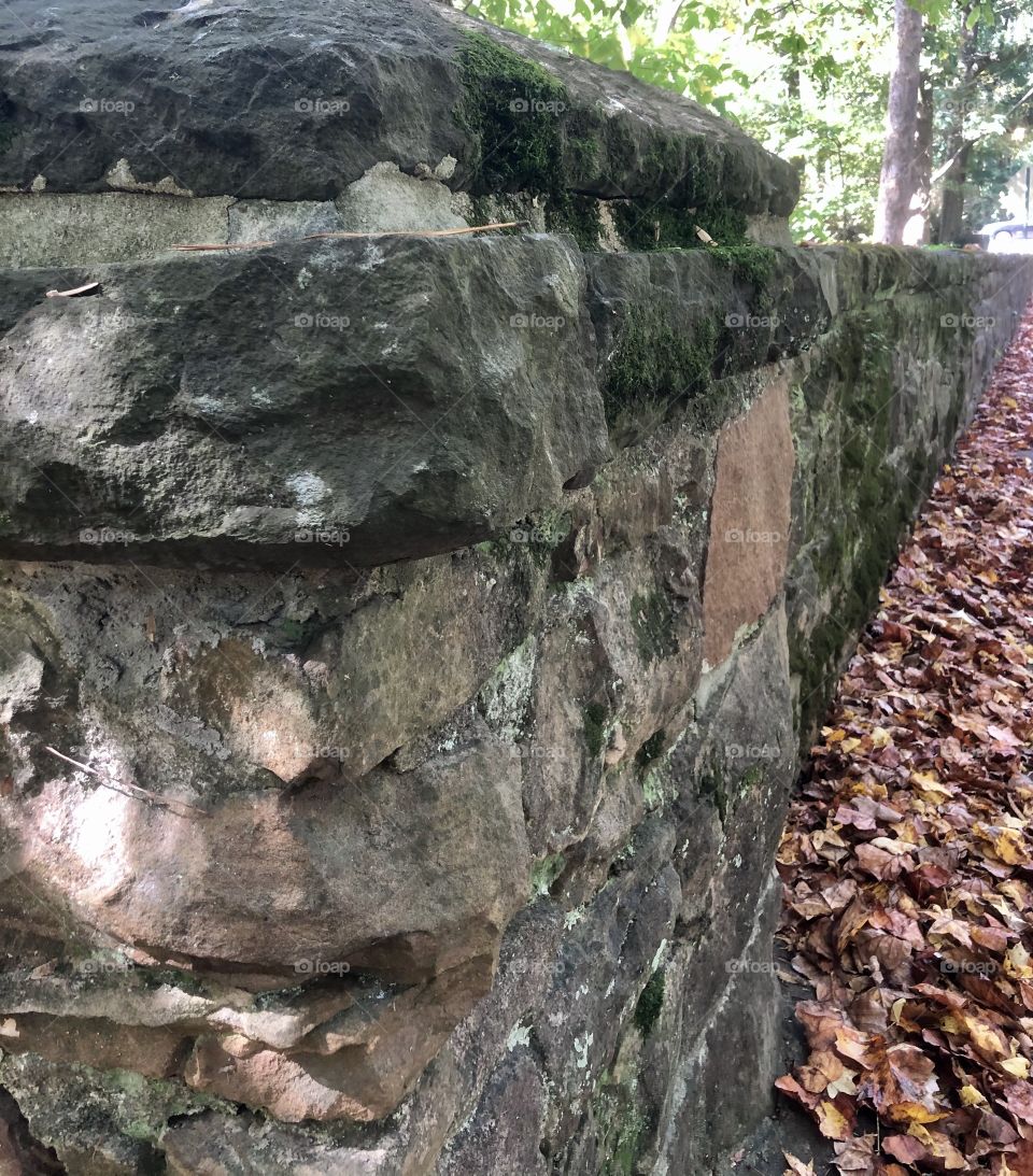 Vanishing perspective of stacked stone wall with fallen leaves blown against it