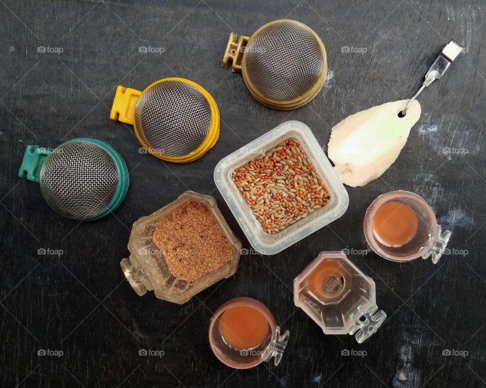 Bird feed with colorful containers. There are round wire nets, factory made bird feed, grains, cuttlefish bones, and also honey containers