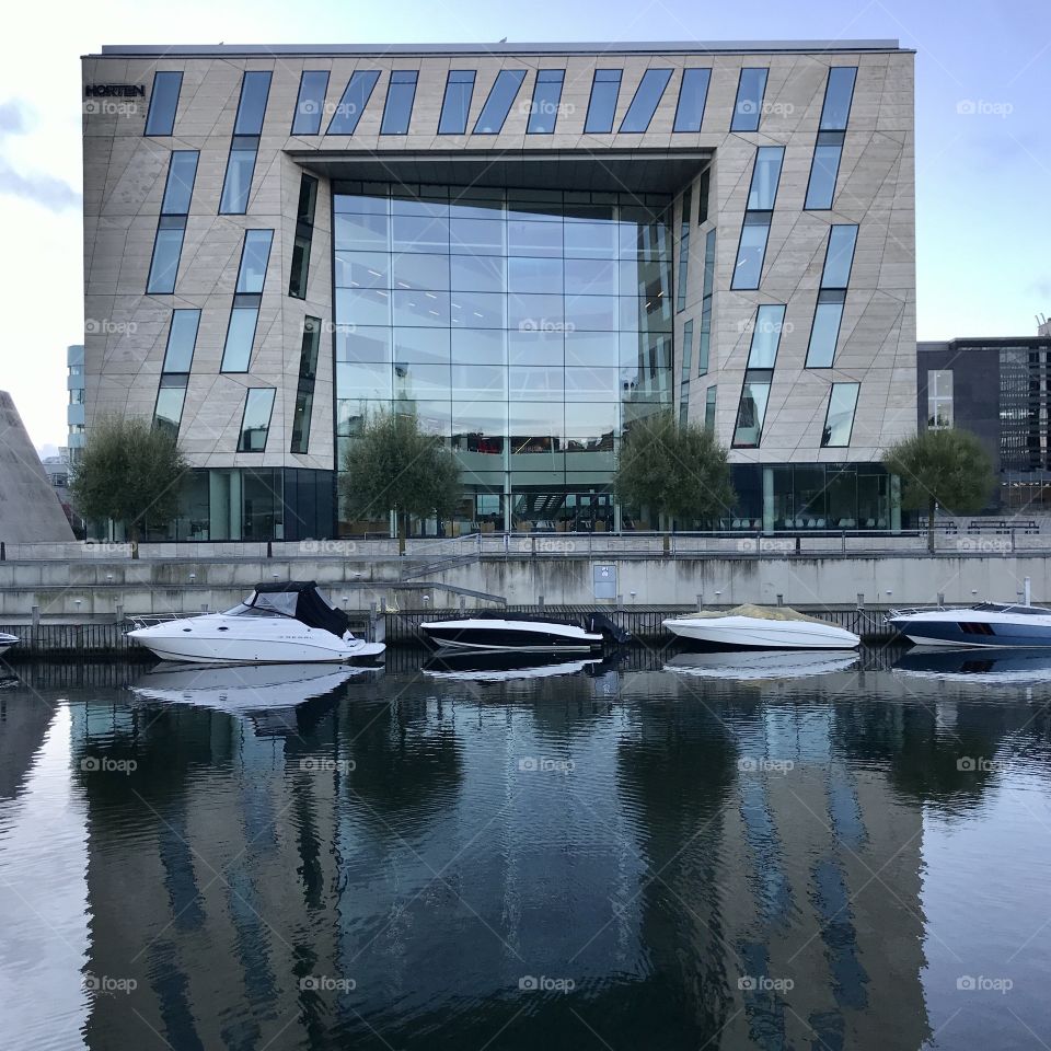 Corporate office building by the waterfront with reflection in the water. Small boats moored by the quay.